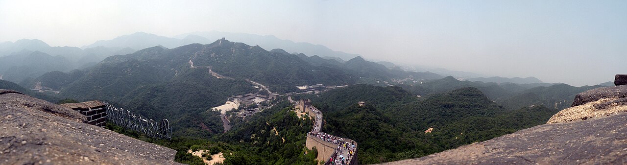 Wide panorama of a long stretch of the Great Wall of China winding over green mountains